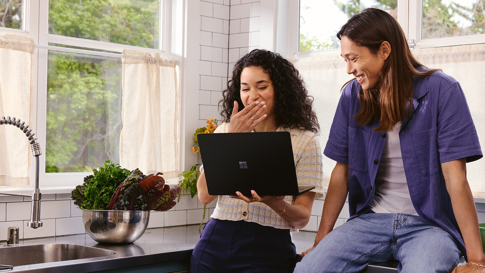 Dua teman menggunakan laptop di dapur.