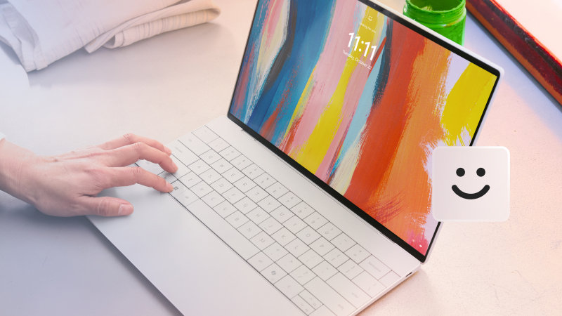 A person’s hands on an open laptop sitting on a desk with a Windows Hello icon on top