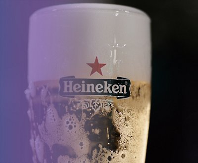 A glass of Heineken beer on a purple and black background.