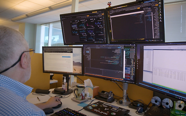 A person working at their desk with five screens displaying data and applications